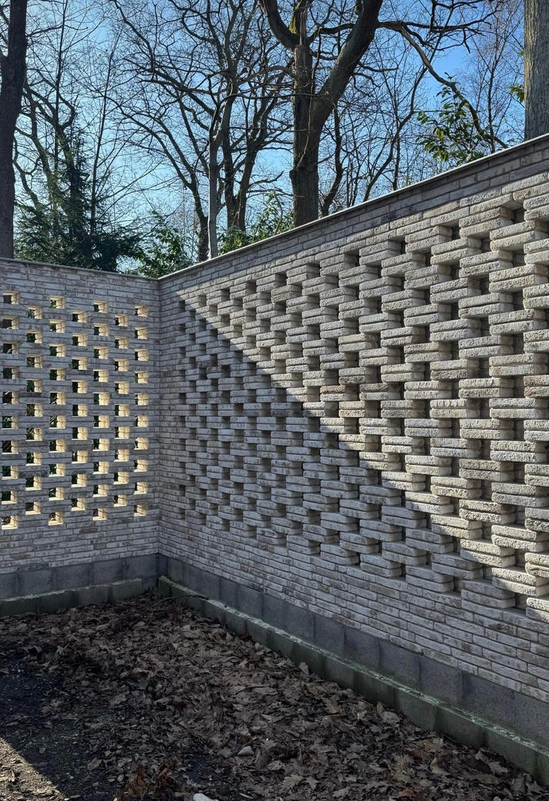 Brick wall with a geometric pattern in an outdoor setting with trees and sky.