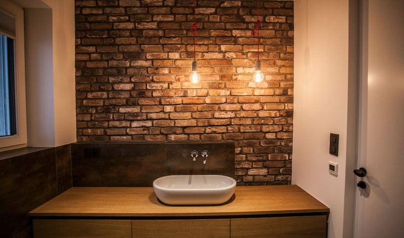 Bathroom with wooden vanity, white sink, and brick wall.